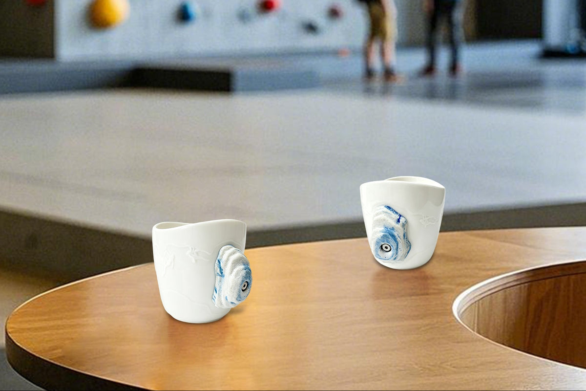 A rock-climbing mug, featuring a handle designed to look like a 3D climbing hold, sits on a table at a bouldering gym.