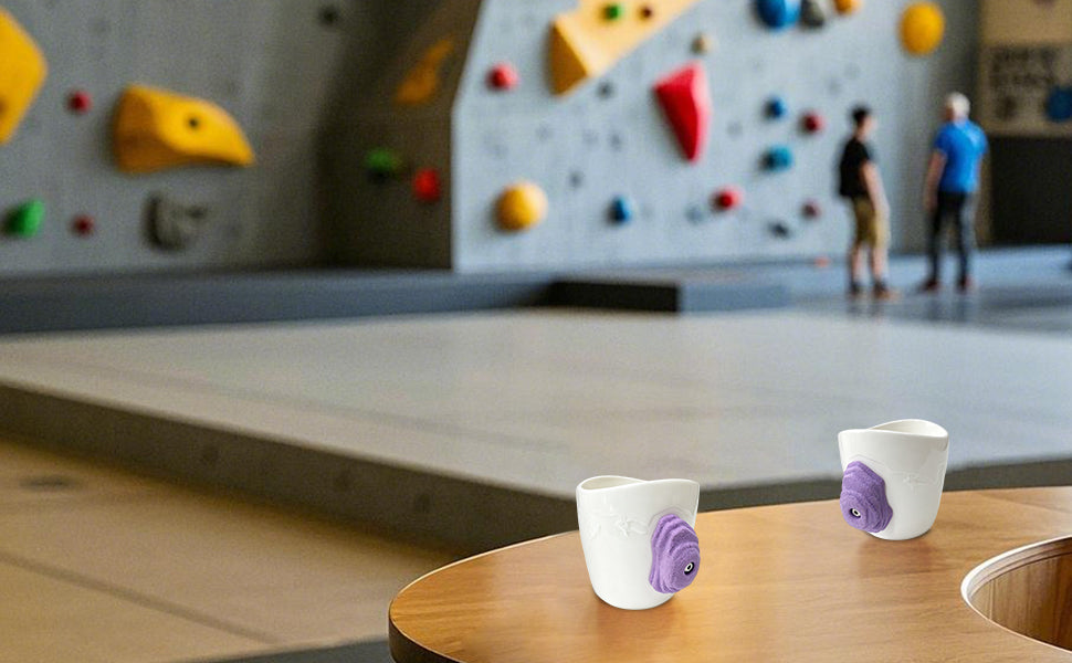 Two Stones rock climbing mug with 3D climbing hold handle displayed in a bouldering gym