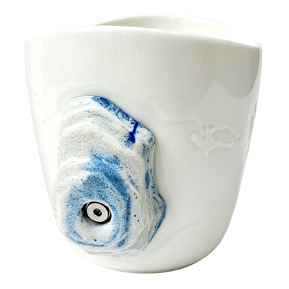 Side view: An off-white ceramic climbing mug, featuring a handle shaped like a 3D climbing hold with blue speckles.