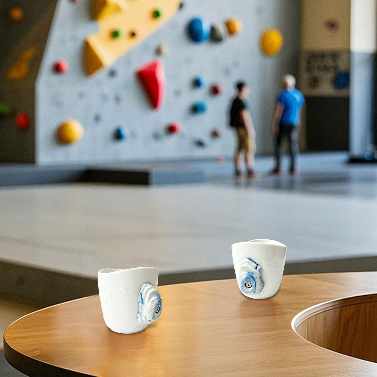 A rock-climbing mug, featuring a handle designed to look like a 3D climbing hold, sits on a table at a bouldering gym.