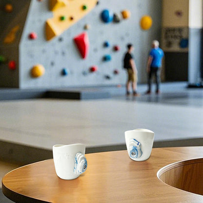 A rock-climbing mug, featuring a handle designed to look like a 3D climbing hold, sits on a table at a bouldering gym.