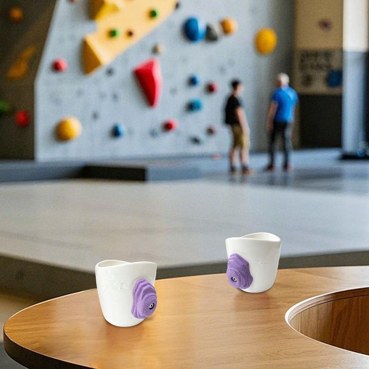 A rock-climbing mug, featuring a handle designed to look like a 3D climbing hold, sits on a table at a bouldering gym.